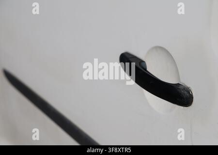 Nahaufnahme eines schwarzen Kunststoff-Außengriffes, der an einer weißen Fahrzeugtür montiert ist. Stockfoto