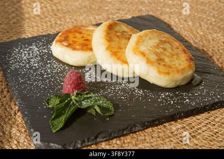 Vanille-Käsekuchen (Hüttenkäse-Pfannkuchen) mit Honig auf einem schwarzen Teller übergossen Stockfoto
