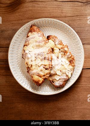 Zwei Mandelkuchen mit geschnittenen Mandeln und Puderzucker belegt, auf einem dekorativen Teller auf einem Holztisch serviert. Ansicht von oben Stockfoto