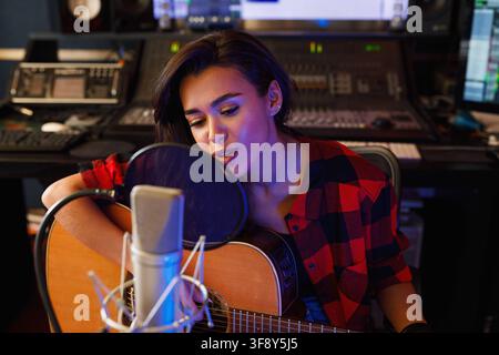 Junge Frau mit Gitarre singt in einem Aufnahmestudio Junge Frau mit Gitarre singt in einem Aufnahmestudio Russland Copyright: xxArtemxVarnitsinx Stockfoto