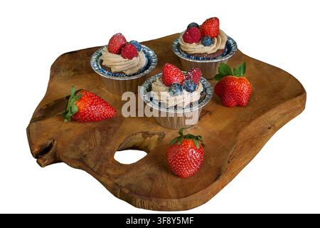 Schokoladen-Cupcakes, die mit Erdbeeren, Blaubeeren und Himbeeren auf einem Holzbrett auf schwarzem Hintergrund dekoriert sind. Hochwertiges Foto Stockfoto