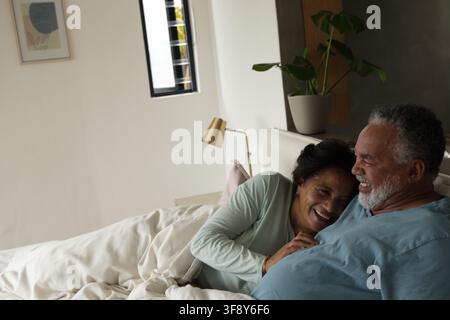 Senioren-Paar afrikanischer Herkunft liegt in einem kuscheligen Schlafzimmer auf dem Bett und hält ein hellrosa Kissen Stockfoto