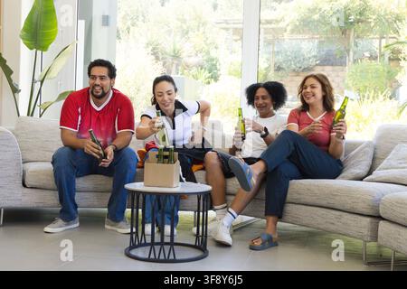 Verschiedene Freunde sitzen in der Lounge auf einer Eckcouch und halten grüne Glasflaschen in der Nähe eines Kartonträgers Stockfoto