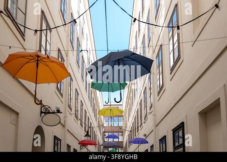 Mehrere farbenfrohe Regenschirme sind über einem schmalen Innenhof zwischen hohen hellen Gebäuden aufgehängt, mit Lichterketten darüber. Stockfoto