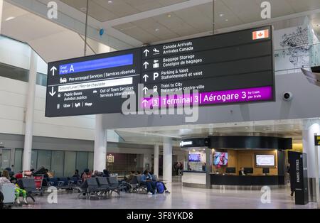 Innenansicht des Toronto Pearson International Airport, zeigt Richtungsschilder und wartende Passagiere. Die Szene fängt die geschäftige Atmosphäre ein Stockfoto