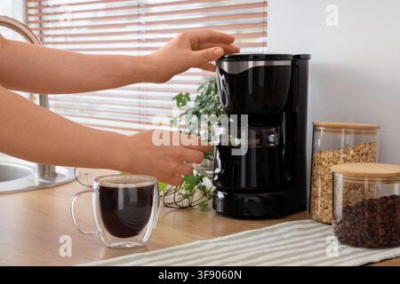 Person, die frischen Kaffee mit einer Filterkaffeemaschine in einer modernen Küche zubereitet, Morgenroutine und Frühstücksgetränk, eine Glas Tasse mit heißem Kaffee steht auf dem Stockfoto