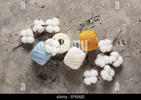 Natürliche Baumwollblüten und bunte Garnspulen auf einem strukturierten grauen Hintergrund, Textil- und Bastelmaterialien Stockfoto