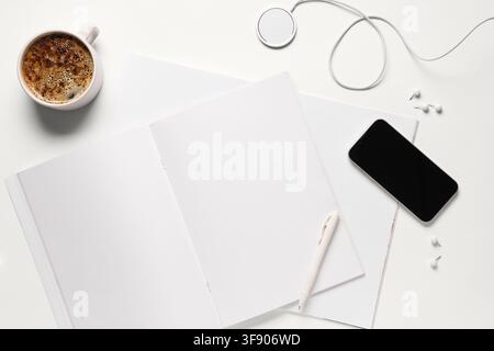 Ansicht von oben eines minimalistischen weißen Schreibtisch-Setups mit einem offenen Notizbuch, Kaffee, Smartphone und kabellosem Ladegerät Stockfoto