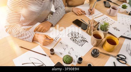 Zwei Personen üben Kalligraphie und Schriftkunst mit Tinte und Pinseln auf einem Holztisch, kreatives Hobby und Kunsterziehung Stockfoto