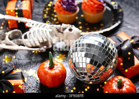 Halloween-Party-Dekorationen mit Diskokugel, Skelett, Cupcakes, Kürbissen und Geschenkschachteln auf dunklem Hintergrund Stockfoto