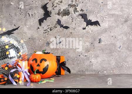 Halloween-Party-Dekorationen mit einem Discokugel, einem Kürbiskandeleimer und Fledermäusen auf einem strukturierten Hintergrund Stockfoto