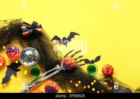 Halloween-Party-Dekorationen mit Skeletthand, Discokugel, Cupcakes und Fledermäusen auf gelbem Hintergrund Stockfoto