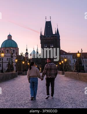 Paar genießt einen romantischen Abendspaziergang auf der Karlsbrücke in Prag. Der Sonnenuntergang wirft ein warmes Licht auf die Stadtlandschaft und unterstreicht den Charme dieses historischen Ortes, der von Touristen bevölkert ist Stockfoto