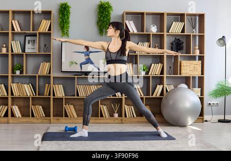 Frau macht Yoga-Krieger-Dehnung im Wohnzimmer, Home-Fitness über TV-Unterricht Stockfoto