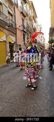 Kostümierter Darsteller tanzt in einem gefiederten Kopfschmuck, während Zuschauer auf einer Straße in Granada, Andalusien, Spanien, am 12. OKT. 2025 zuschauen. Stockfoto
