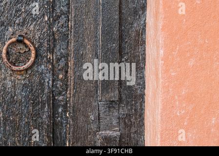 Nahaufnahme einer alten dunklen Holztür mit einem rostigen Metallring und einer Terracotta-Wand Stockfoto
