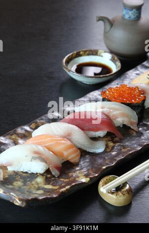 Eine Auswahl an Nigiri-Sushi-Stücken, die auf einem stilisierten Teller mit einer kleinen Schüssel Dip-Sauce angeordnet sind Stockfoto