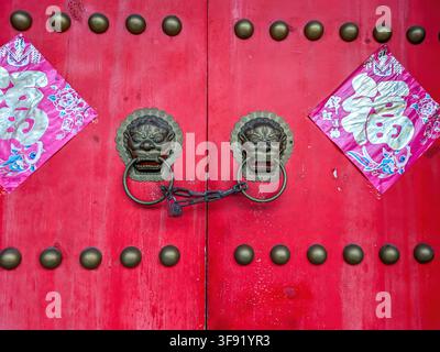 Rote Holztüren mit kunstvollen Metall-Löwengriffen. Stockfoto