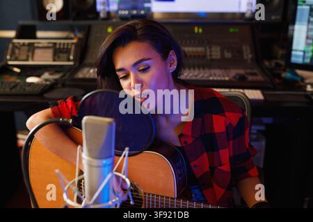 Junge Frau mit Gitarre singt in einem Aufnahmestudio Stockfoto
