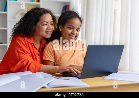 Lächelnde schwarze Mutter hilft ihrer Tochter bei den Hausaufgaben am Laptop Stockfoto