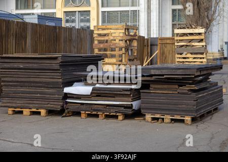 Stapel dunkler Holzplatten, die im Freien auf Versandpaletten gelagert sind, zeigen organisierte Baumaterialien und veranschaulichen Konzepte des Lagerbestandsmanagements, comme Stockfoto