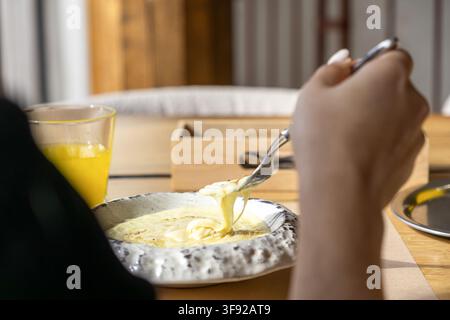 Person, die heiße Kartoffelpüree mit zähflüssigem Käse in einer strukturierten Keramikschale genießt, aufgenommen in einer Tischgestaltung, die eine warme Atmosphäre vermittelt Stockfoto