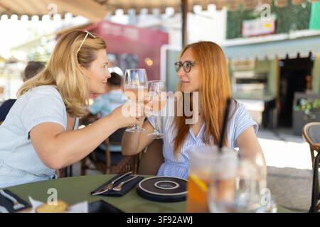 Zwei Frauen genießen Getränke in einem Café in einer geschäftigen Außengestaltung an einem sonnigen Tag Stockfoto