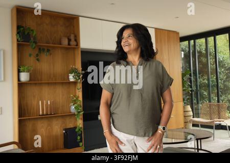 Afroamerikanische Frau steht im Wohnzimmer und trägt eine olivgrüne Bluse in der Nähe von Einbauschränken Stockfoto