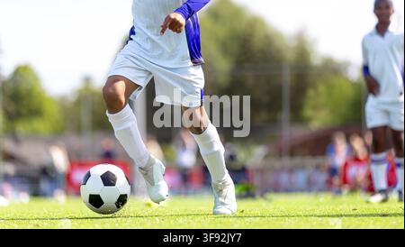 Niedrigwinkelaufnahme eines Junior-Fußballspielers, der den Ball auf dem Spielfeld dribbelt – Nahaufnahme der Fußarbeit und der Fußballschuhe während eines Jugendfußballspiels Stockfoto