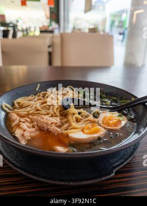 Köstliche japanische Hühner-Ramen-Nudeln mit einer reichhaltigen Brühe und cremigem Ei in einer matten schwarzen Schüssel auf einem Holztisch, perfekt für die Förderung von Dini Stockfoto