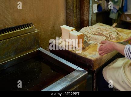 Handgefertigte Fischkuchen-Zubereitung mit Fischpastenformen auf einem Holzschneidebrett neben einer kommerziellen Öl-Heißluftfritteuse in einem lokalen Marktstand. Stockfoto