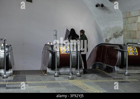 Paar wartet in der Nähe einer Metrotreppe, fängt einen Moment des städtischen Pendelns und der Stadterkundung in einem stoischen öffentlichen Raum ein, betont Infrastruktur Stockfoto