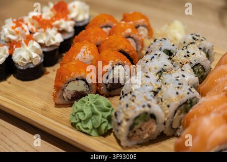 Eine vielfältige Auswahl an frischen Sushi-Rollen mit rohem Fisch, Sesamsamen und scharfem Wasabi, arrangiert auf einem Holzbrett, betont den visuellen Reiz Stockfoto