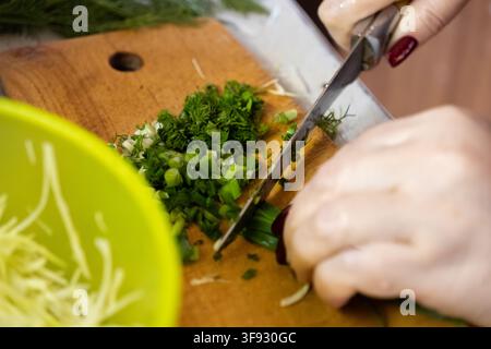Hände schneiden aromatische Kräuter auf einem strukturierten Holzbrett, um den handwerklichen Prozess der Lebensmittelzubereitung für das Kochen von frischen, biologischen und nahrhaften Gerichten hervorzuheben Stockfoto