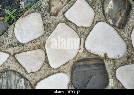 Nahaufnahme von unregelmäßig geformten weißen und dunklen Steinen, die in Beton eingebettet sind, und zeigen kontrastierende Texturen und natürliche Muster für dekorative Böden o Stockfoto