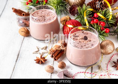 Gewürzter Schokoladen-Eierlikör-Punsch-Cocktail, serviert mit Zimtstab, Muskatnuss und Schokolade, auf gemütlichem Weihnachtshintergrund Stockfoto