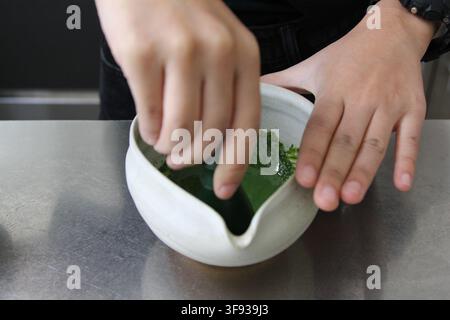 Rühren von leuchtend grünem Matcha-Tee in einer Keramikschüssel auf einer sauberen Arbeitsplatte. Stockfoto