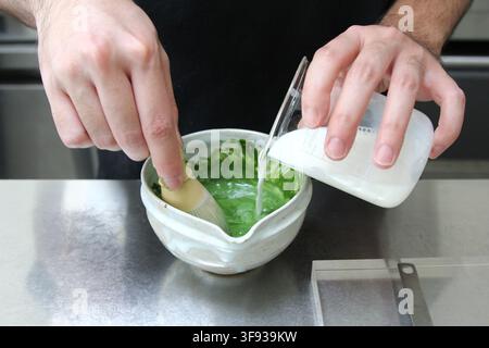 Milch in eine Keramikschüssel gießen und Matcha-Grüntee mit einem Bambusquirl verquirlen. Stockfoto