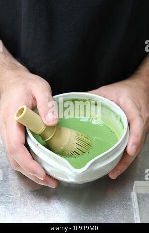 Eine Person rührt Matcha-Grüntee in einer traditionellen Keramikschale mit einem Bambusrührer. Stockfoto