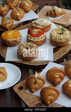 Eine Ansicht von oben verschiedener frisch gebackener Gebäckstücke, Croissants und farbenfroh verzierten Donuts, die auf Holzservierplatten angeordnet sind. Stockfoto