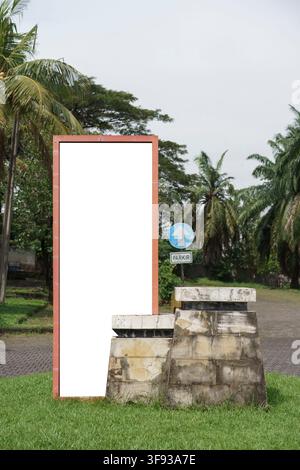 Ein vertikales weißes leeres Werbetafeln auf einem steinernen Sockel, bereit für Werbemodelle, steht im Freien auf einem grünen Rasen umgeben von Palmen Stockfoto