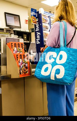London UK, 14. August 2026, Unerkennbare einsame Frau mit einer Co-Op-Tragetasche, die an der Kasse von Waitrose auf die Bezahlung wartet Stockfoto
