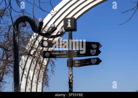 Kiew, Ukraine - 15. März 2026: Stadtstraßenschild mit Wegweisungen zu lokalen Attraktionen und einem modernen Bogenmonument im Hintergrund, hochlig Stockfoto
