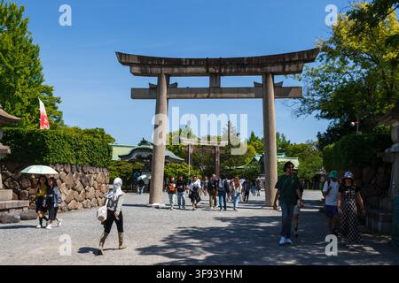 Touristen gehen durch ein antikes Steintorii-Tor am Hokoku-Schrein im Park von Osaka Castle in Japan. Stockfoto