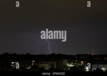 Ein Blitzstrahl erhellt eine dunkle Wolke in einer nächtlichen Stadtsilhouette. Stockfoto