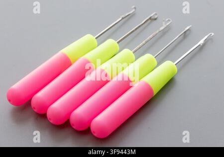 Fünf farbenfrohe Häkelhaken-Werkzeuge sind ordentlich auf einem grauen Hintergrund angeordnet Stockfoto