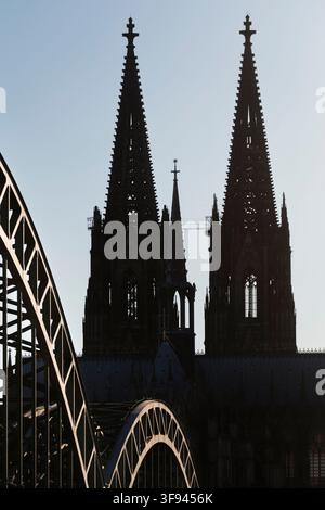 Hochformat-Außenaufnahme zeigt die beiden markanten Haupttürme und den Vierungsturm des Kölner Doms im Gegenlicht. Im Vordergrund erheben sich die ges Stockfoto