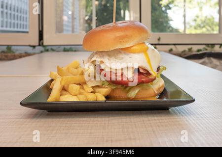 Spießburger mit flüssigem Spiegeleier und Pommes auf einem Außenterrassentisch serviert Stockfoto
