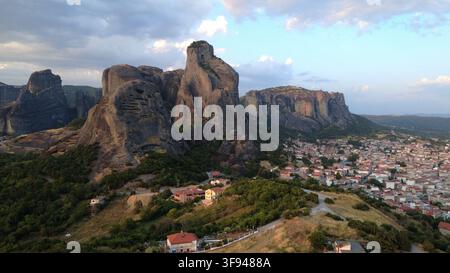 Luftaufnahme der dramatischen Meteora-Felsformationen, die bei Sonnenuntergang über einer traditionellen griechischen Stadt aufragen, umgeben von üppigen grünen Wäldern Stockfoto