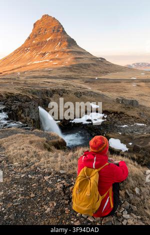 Abenteuerlustige Fotografin im Winter in Island, die am Kirkjufell-Wasserfall sitzt Stockfoto